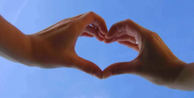 Person making a heart with their hands in front of a blue sky